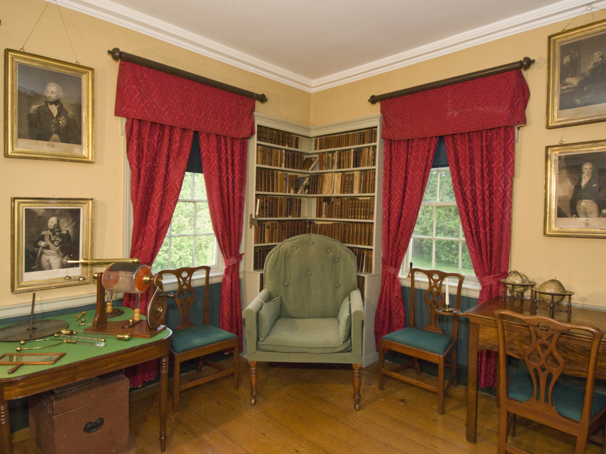 library featuring a tall bookcase, several paintings, and a table with a telescope-like device.