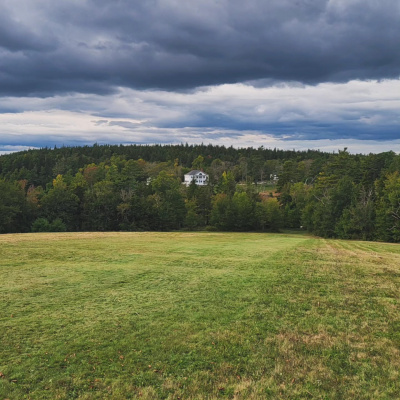 Uniacke Estate in the distance, a grand white house with a classical design, including a columned entrance and a long veranda. The house is surrounded by a well-maintained lawn and mature trees.